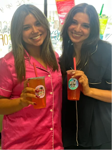 Two smiling customers holding fruit teas by the window at Restore Nutrition
