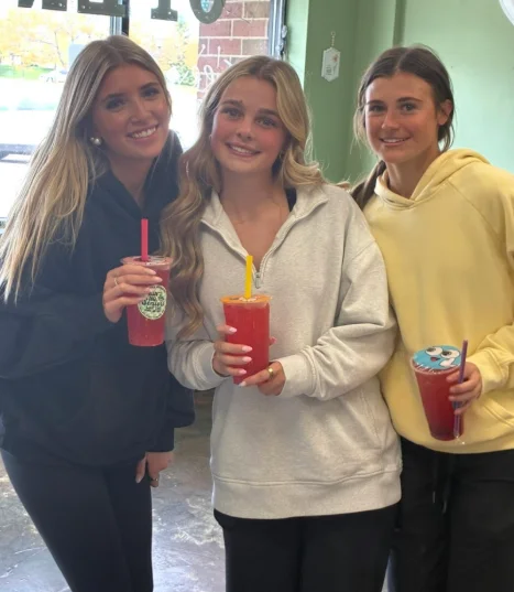 Three friends holding red shakes inside Restore Nutrition in Plymouth, MN