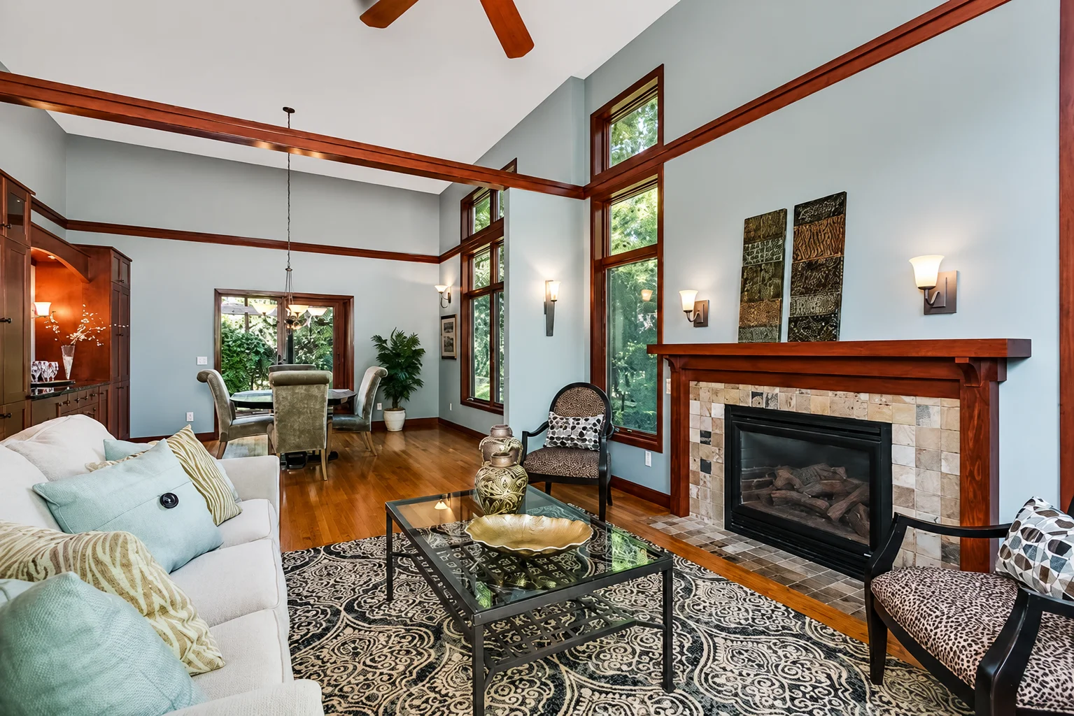 Open-concept living room painted in a soft blue-gray with rich wood trim, fireplace surround, and vaulted ceiling.