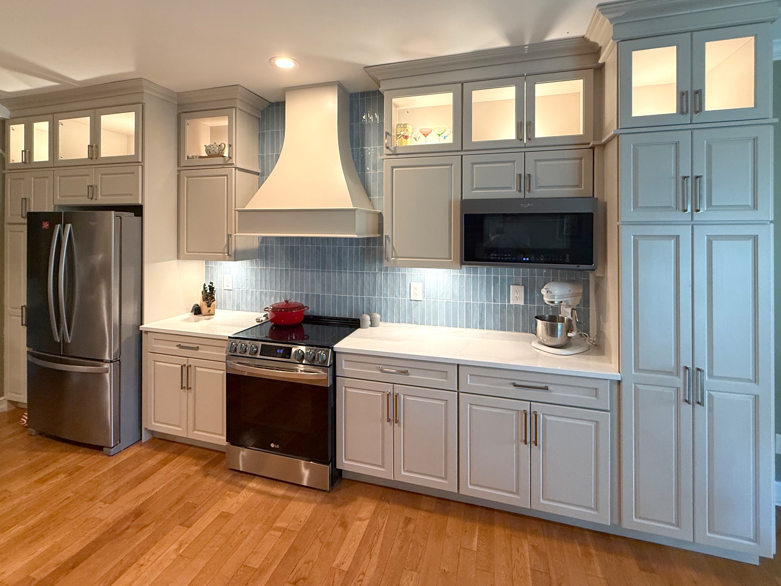 Completed kitchen remodel in Fairfield Harbor, New Bern, featuring light gray cabinetry, quartz countertops, a blue tile backsplash, and a custom range hood.