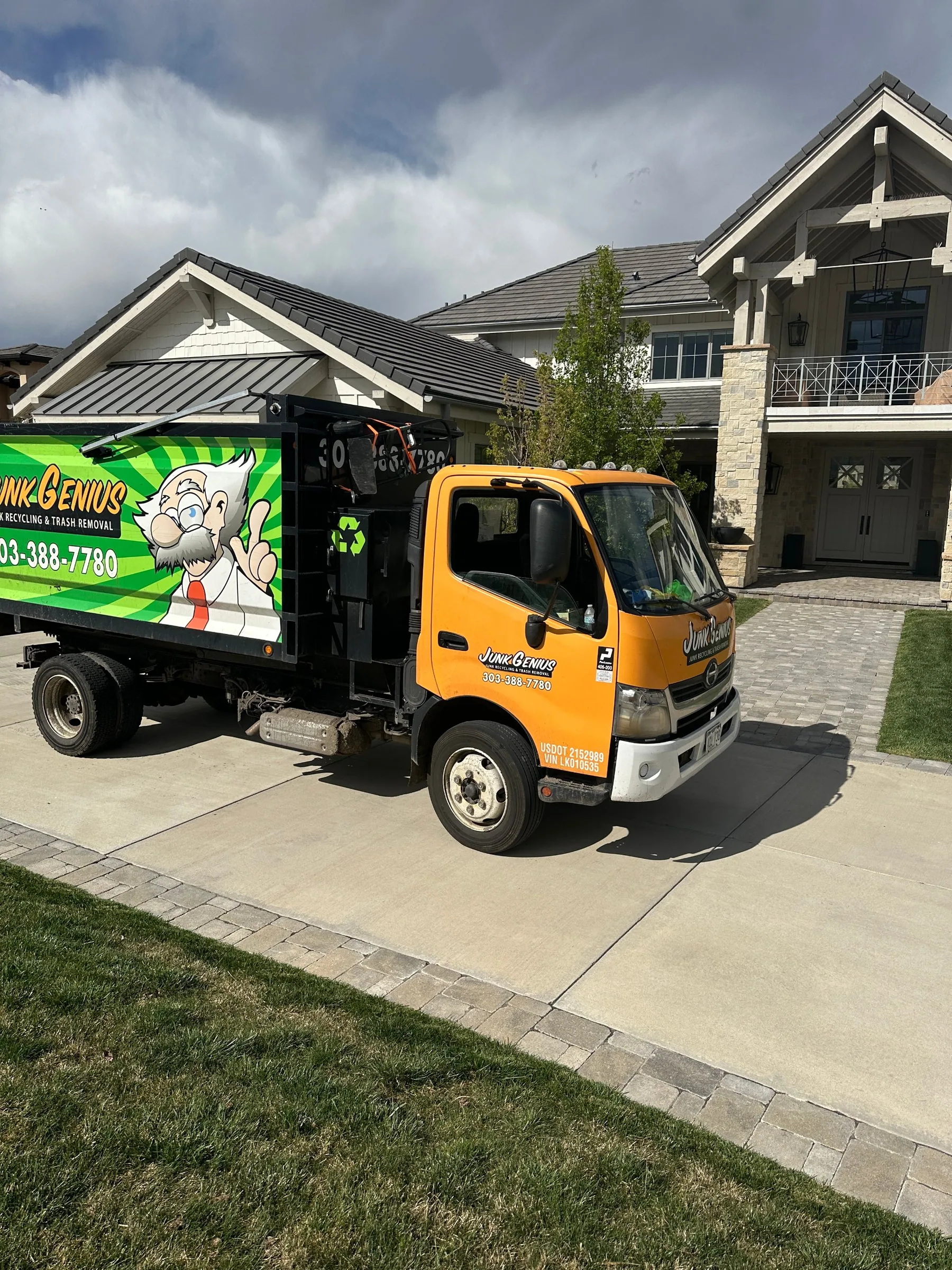 Junk Genius truck parked in a residential driveway outside a home, ready for a retail and residential junk removal pickup.