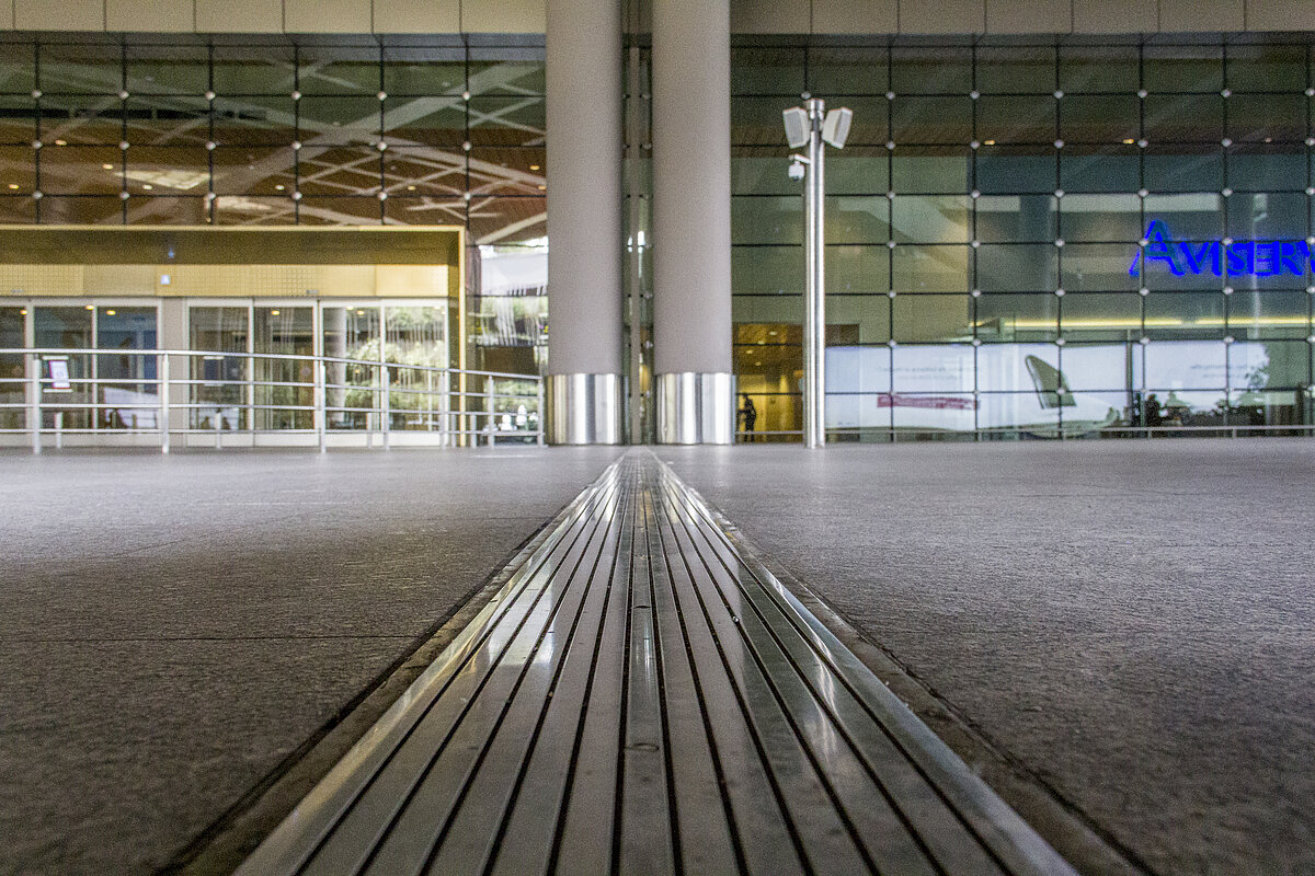 Metal expansion joint running from the foreground into a glass-fronted airport terminal building
