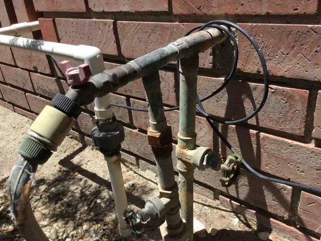 Outdoor pipe connections at a brick wall by Graham Plumbing