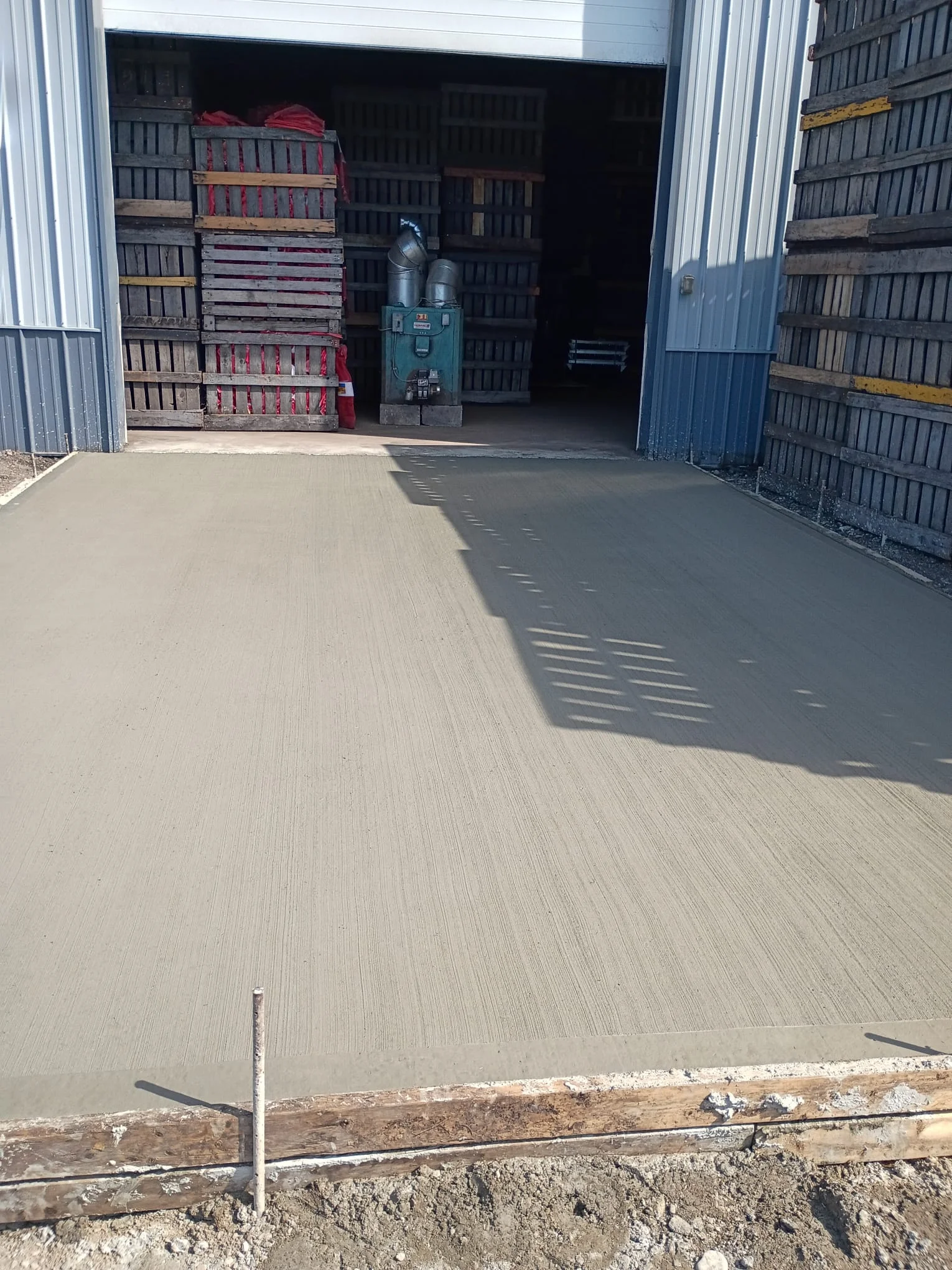 Concrete driveway and entryway pour in progress at a commercial facility with storage structures.