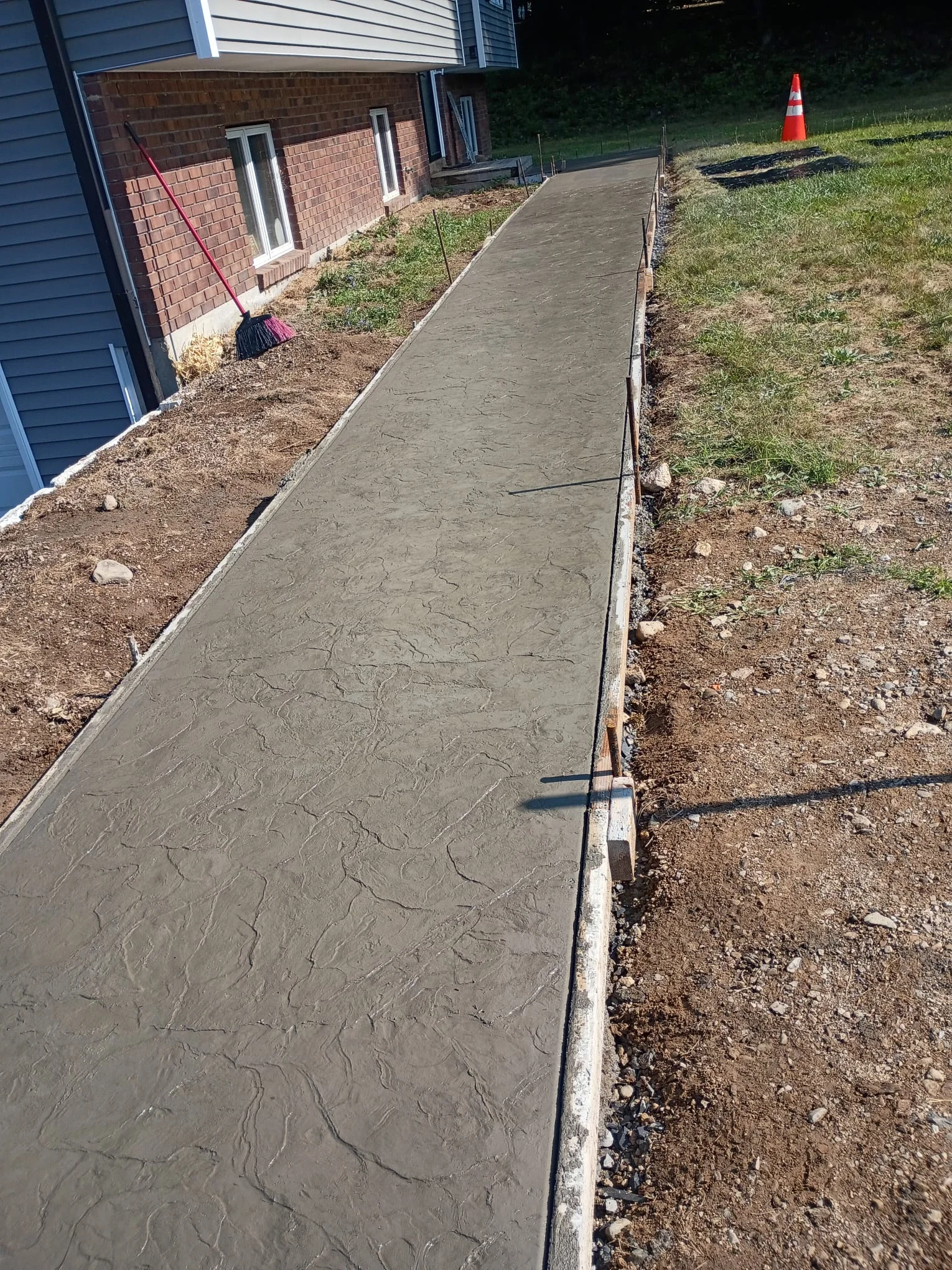Concrete sidewalk pour in progress at a residential property exterior, with forms and freshly finished concrete surface.