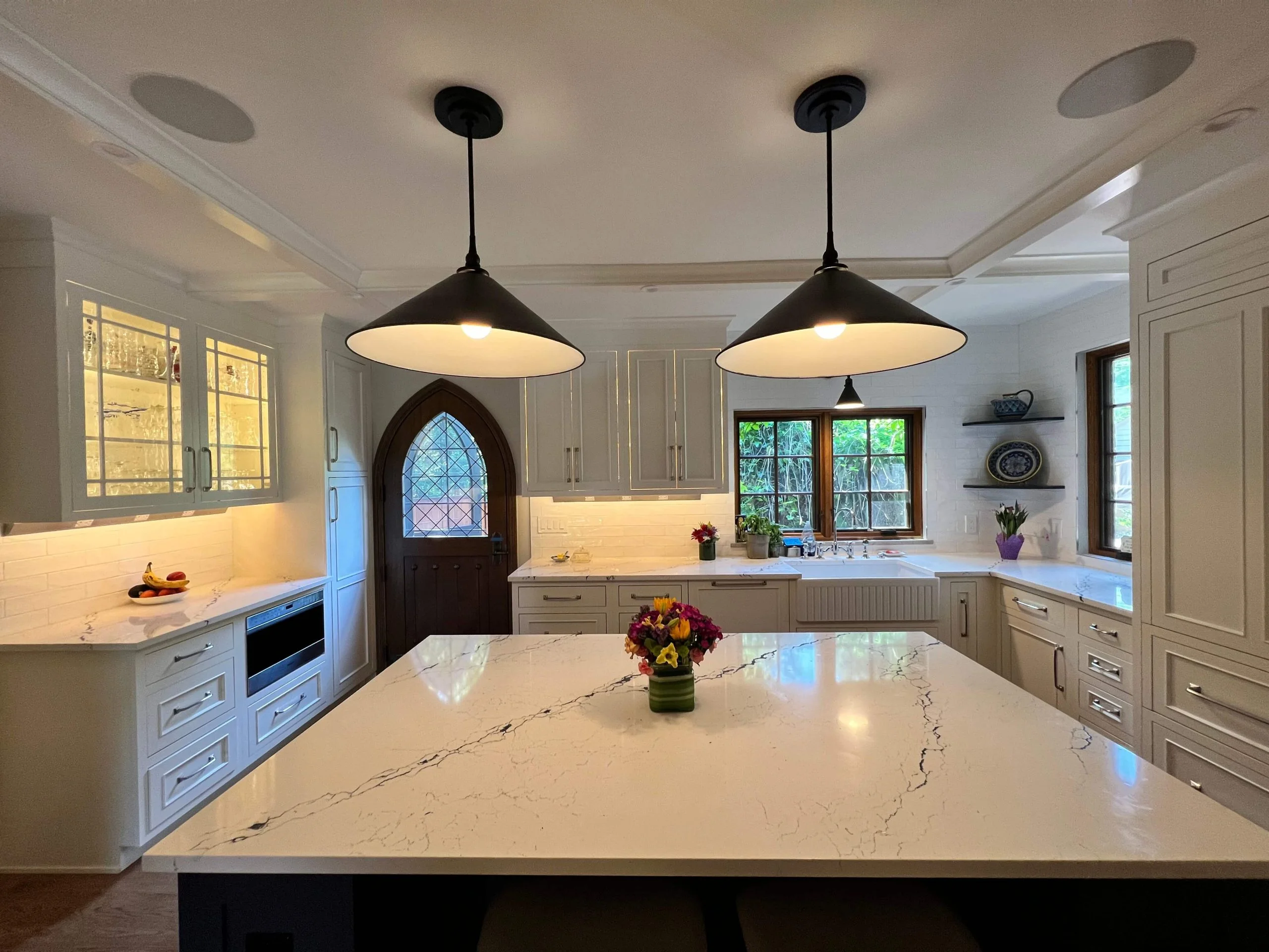 Pendant lighting fixtures installed in a modern kitchen with white cabinetry and marble countertops.