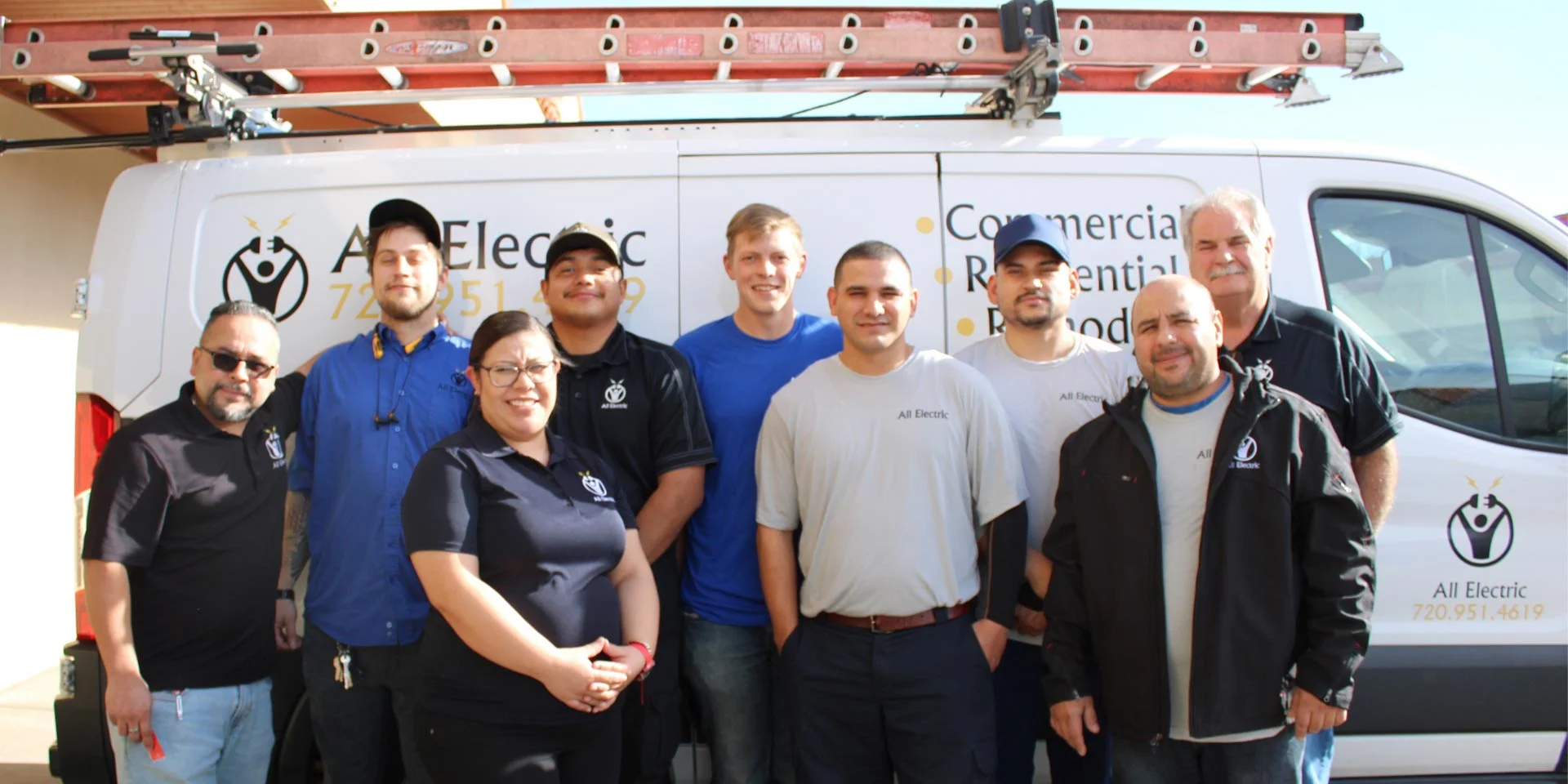 A team of electricians posing in front of an All Electric service van equipped with a roof ladder rack, showcasing the company's commercial and residential electrical services.