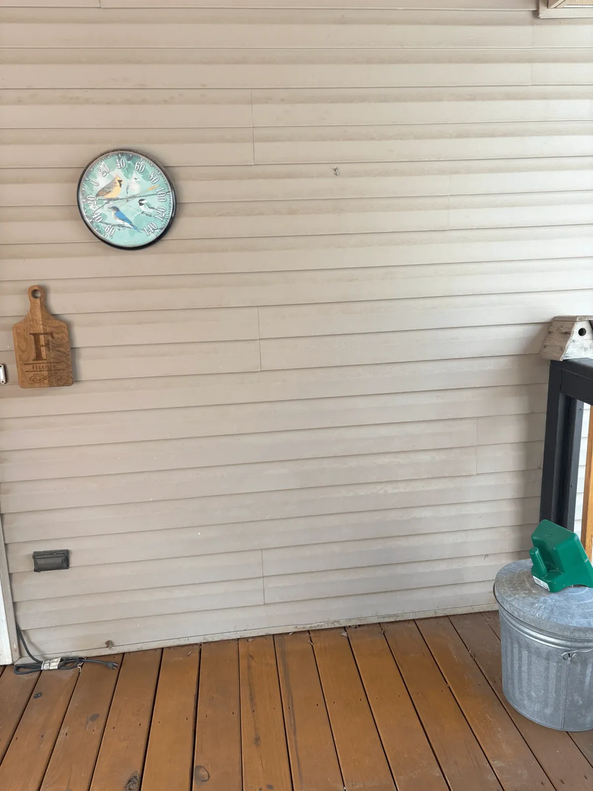 A residential deck or patio space with an outdoor electrical outlet and weatherproof enclosure mounted on a cream-colored siding wall.
