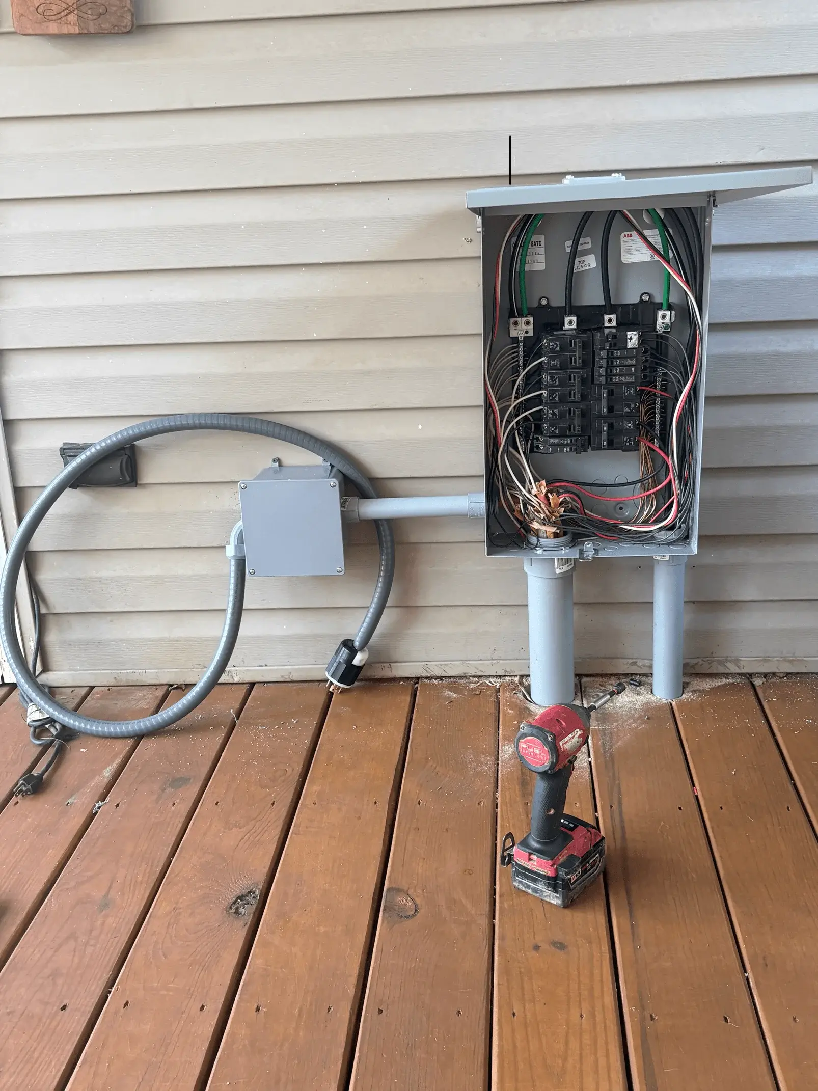 Electrical panel upgrade installation on a residential deck, showing a completed main service panel with conduit and breaker connections.