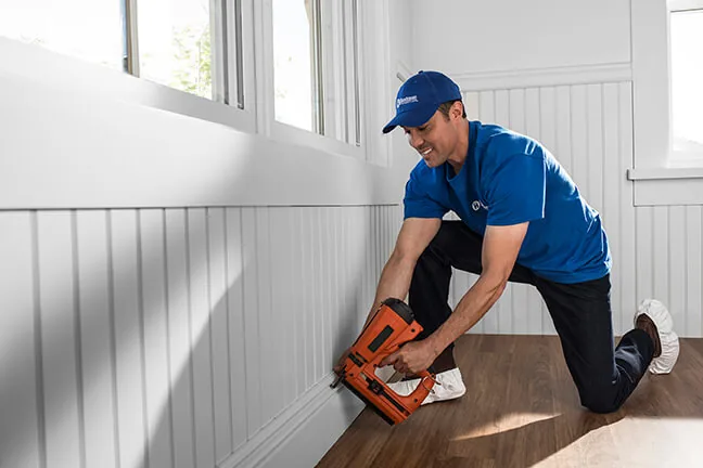 Craftsman nailing baseboard below wainscoting