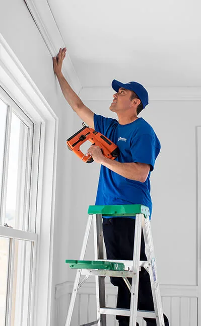 Craftsman on a ladder nailing crown trim at the ceiling