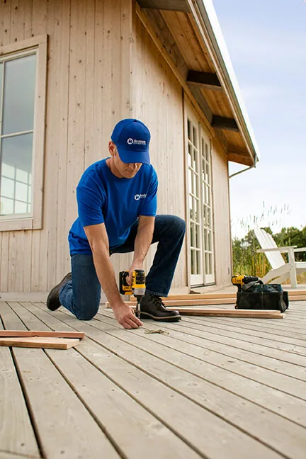 Craftsman kneeling on a wood deck beside a cabin wall