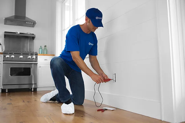 Craftsman kneeling to work on a wall outlet