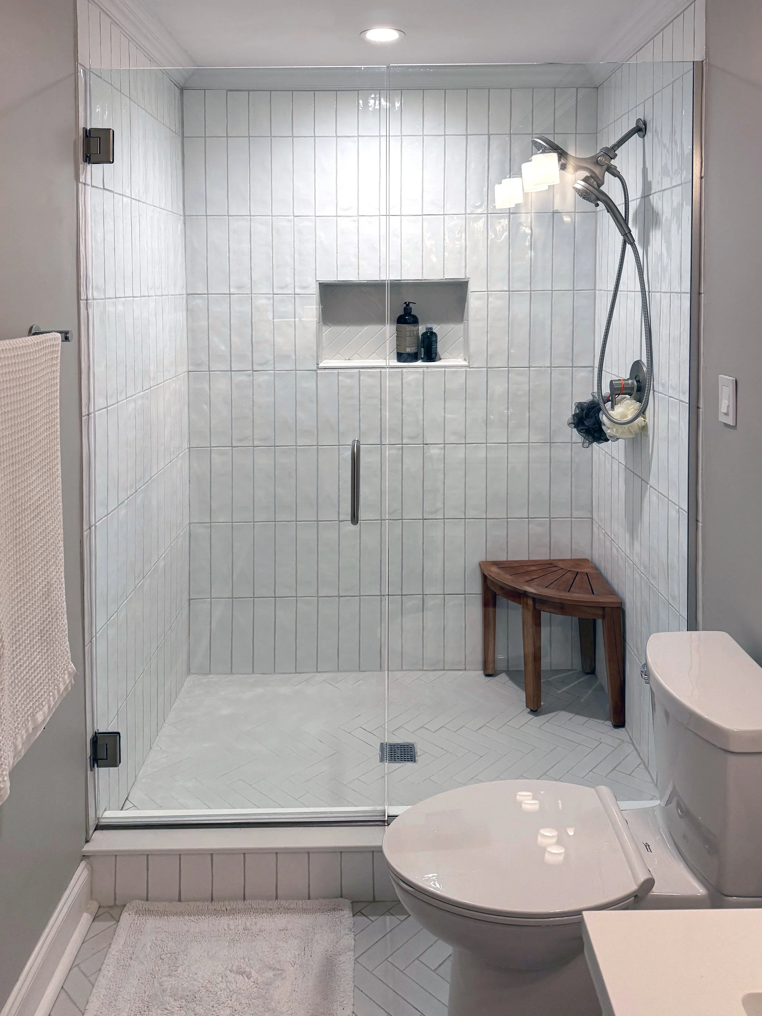 A complete walk-in shower with vertical subway tile walls, glass enclosure, and marble floor in a modern bathroom remodel.