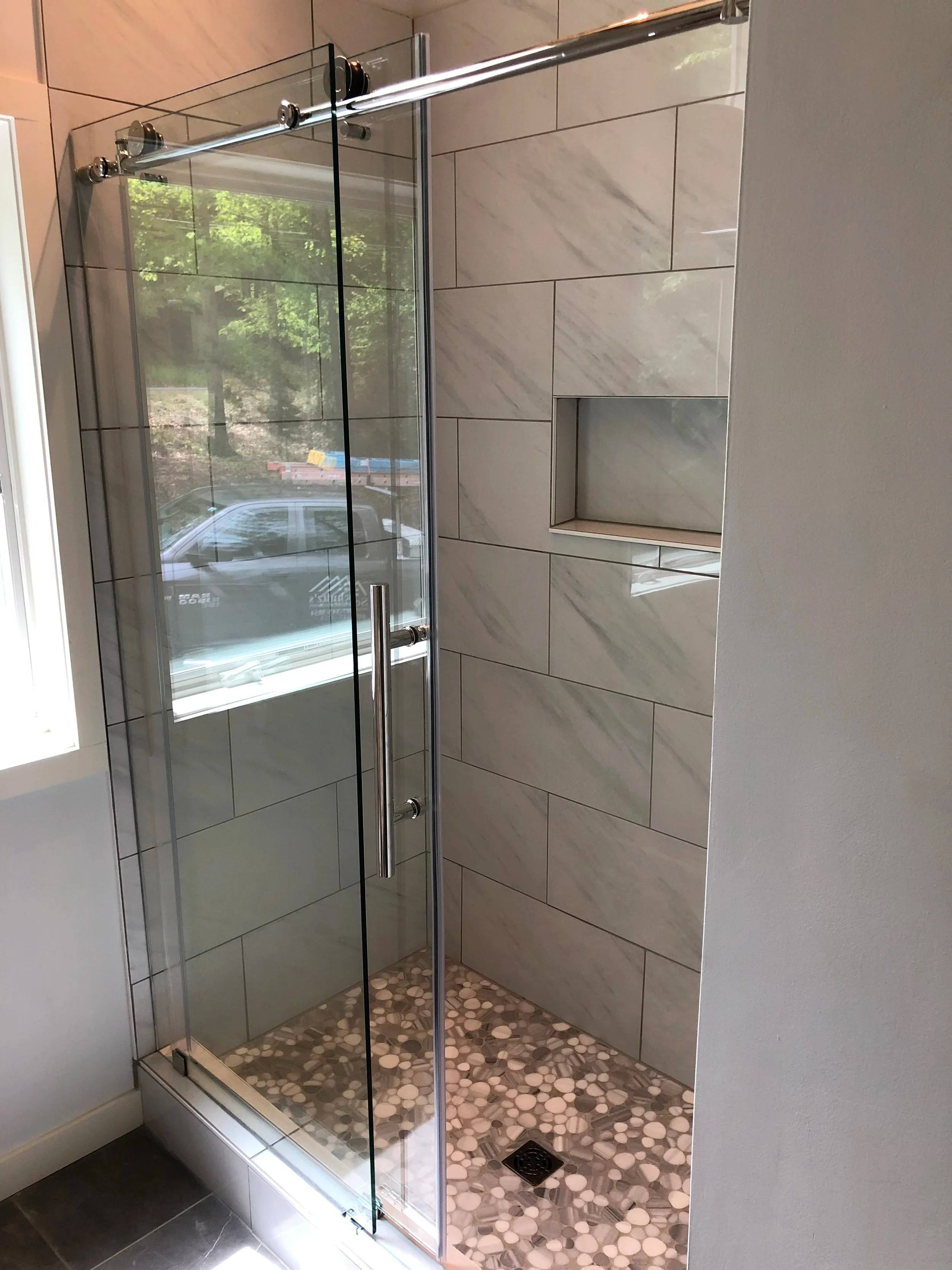 A frameless glass shower enclosure with sliding door and stone tile surround in a modern bathroom.