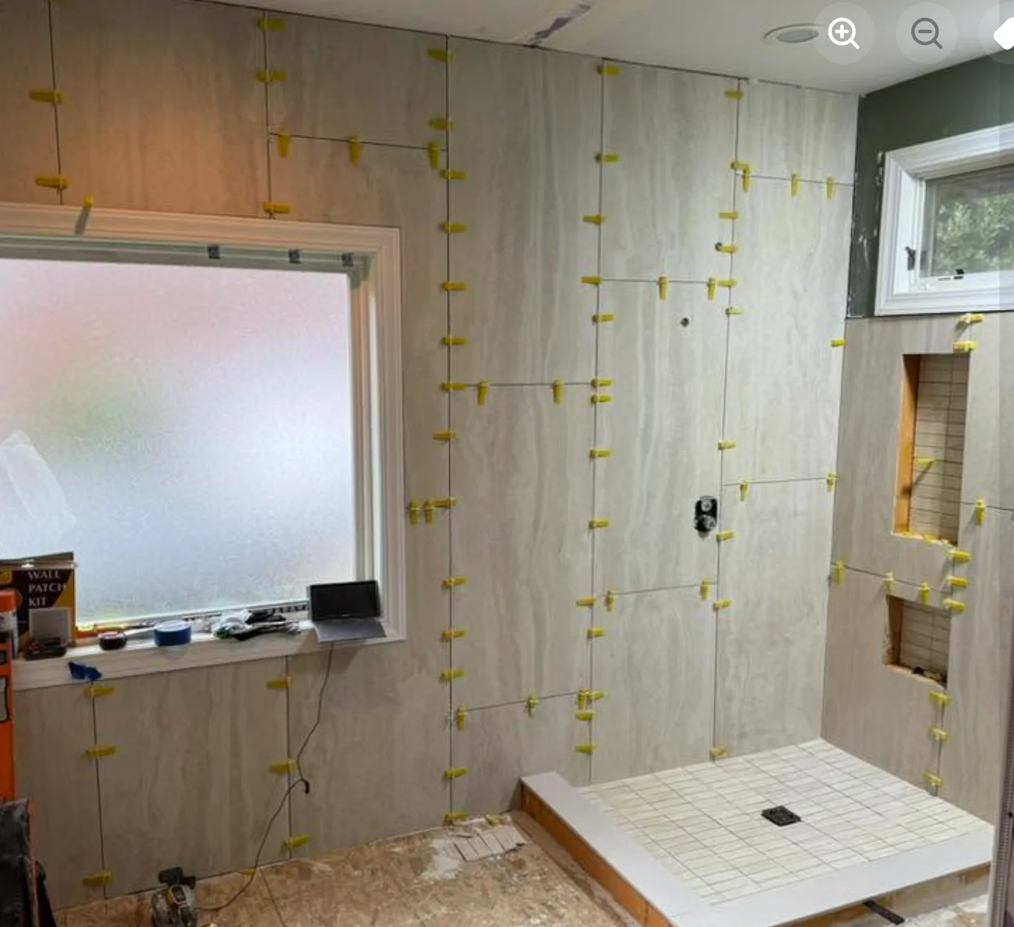 Tile installation and waterproofing work in progress on a bathroom shower enclosure, showing drywall preparation with spacers and leveling guides.