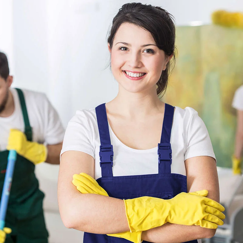 A cleaning service worker wearing protective gloves and uniform apron poses for a portrait in an indoor setting.