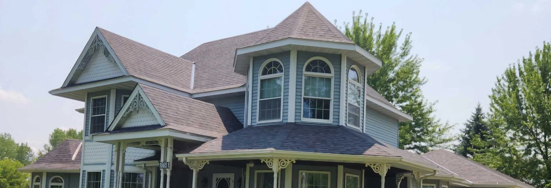 Residential roof installation featuring multiple roof lines, dormers, and architectural details on a two-story Victorian-style home surrounded by landscaping.