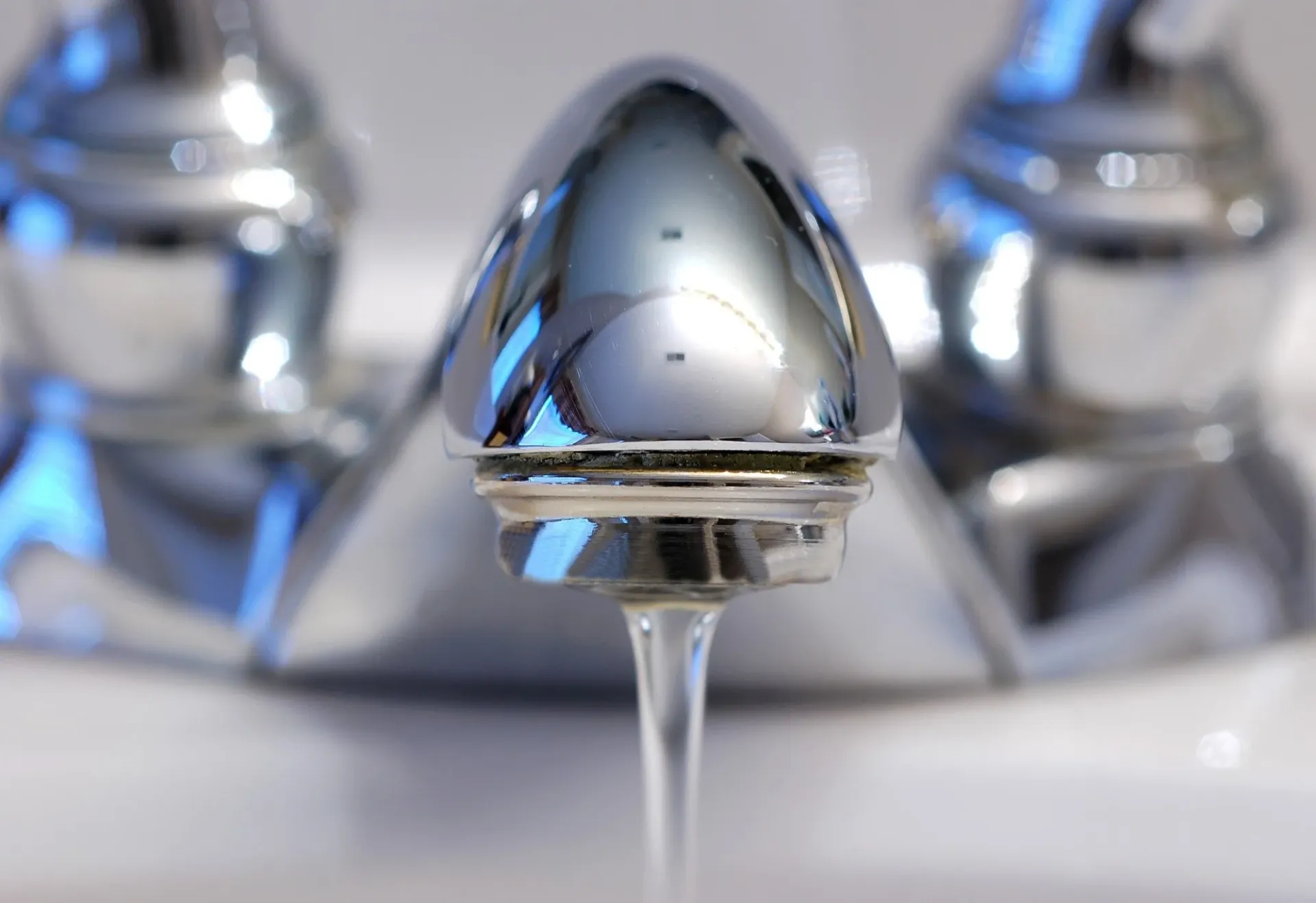 Chrome faucet aerator or valve component in close-up detail, showcasing polished metalwork and water droplet.