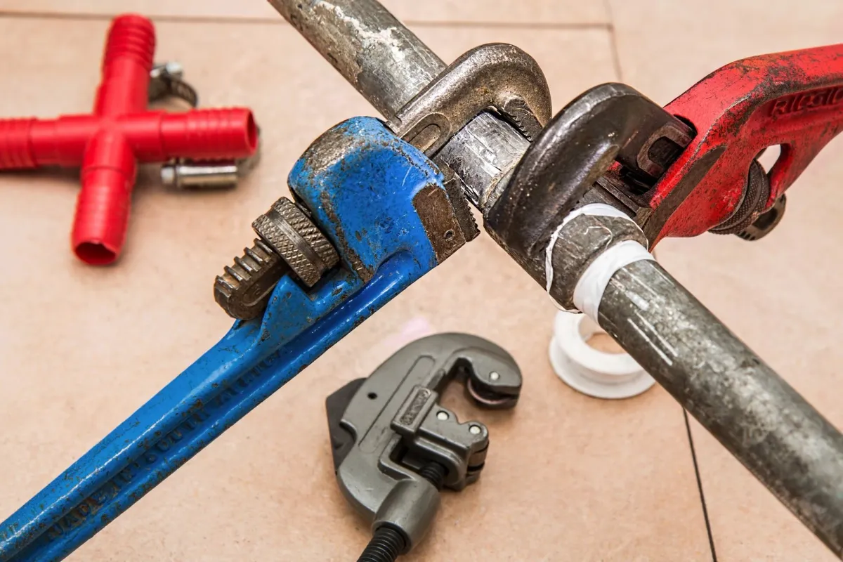 Pipe wrench and other plumbing tools positioned on a metal pipe with white tape and fittings during repair work.