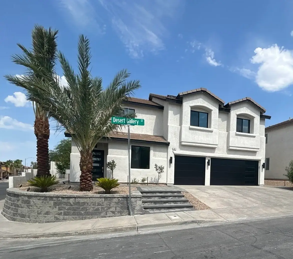 Residential front yard landscaping with a mature palm tree, retaining wall, and drought-resistant planting in a desert suburban setting.