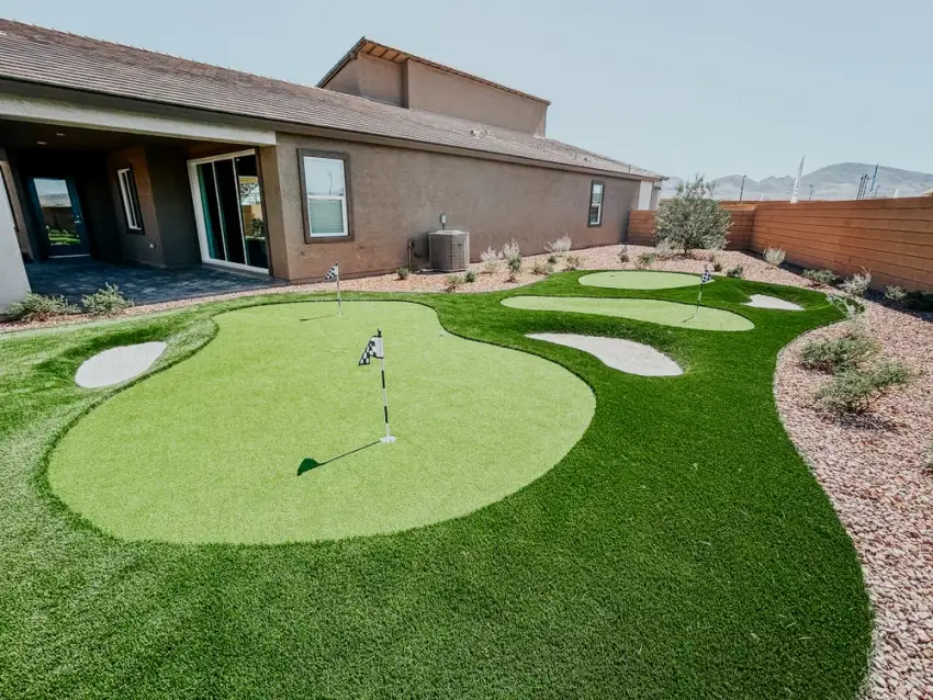 Synthetic putting green with bunkers and landscaping in a residential backyard next to a modern home.