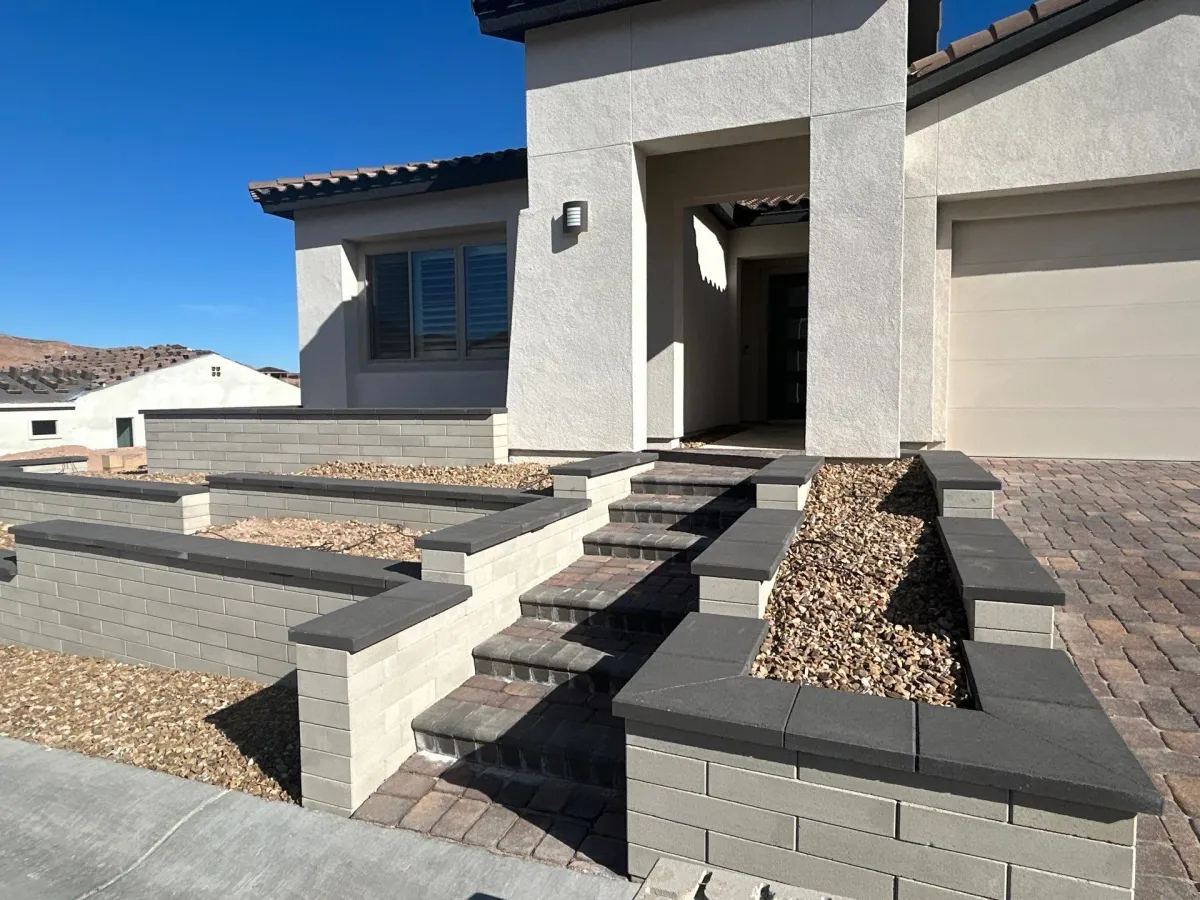 Retaining walls and tiered hardscape landscaping with gravel fill in a residential front yard entry area.