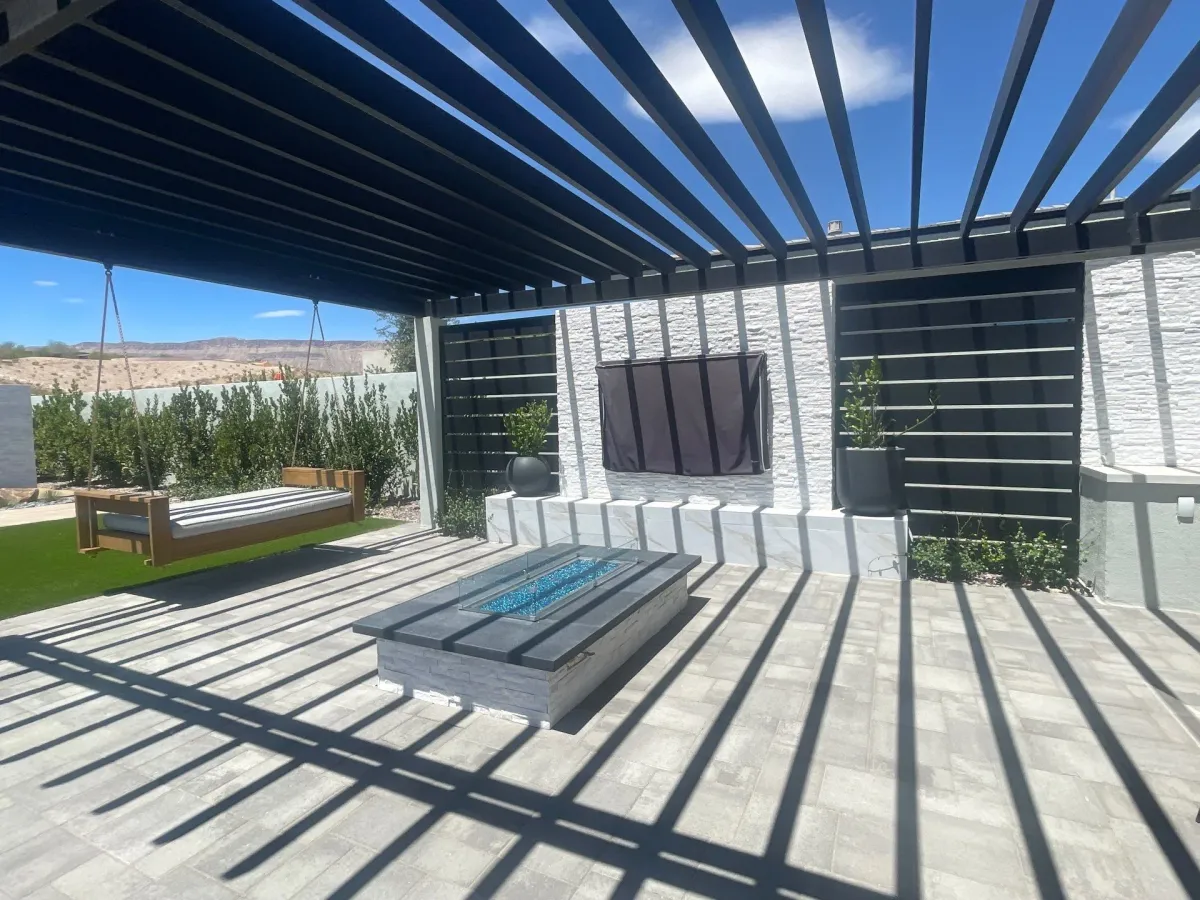 A modern hardscape patio with pergola, fire pit, and built-in seating in a residential backyard setting.