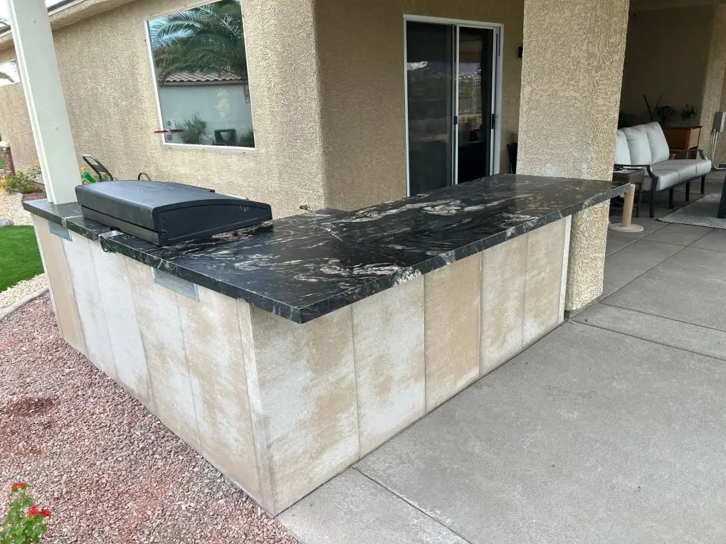 Custom outdoor kitchen with black marble countertop and built-in grill in a residential patio hardscape setting.