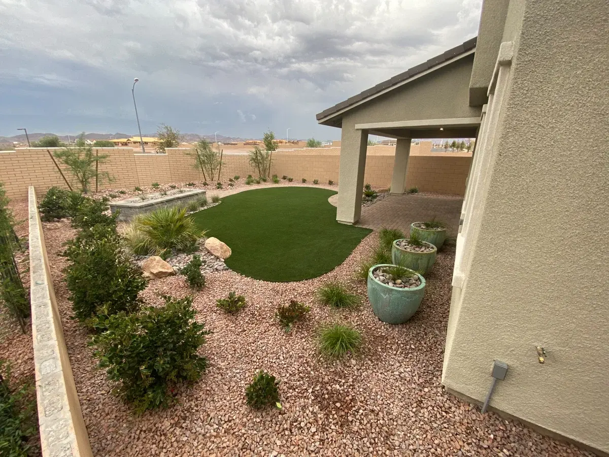 Artificial turf lawn installation in a residential backyard with xeriscaping and decorative hardscape elements.