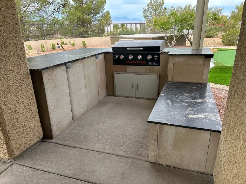 An outdoor kitchen with a Blackstone griddle and built-in cabinetry in a residential backyard patio setting.