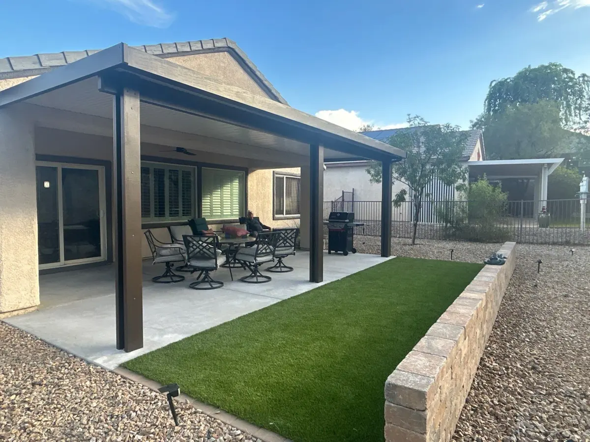 A patio and lawn installation with artificial turf, concrete paver surface, and a modern pergola structure in a residential backyard setting.