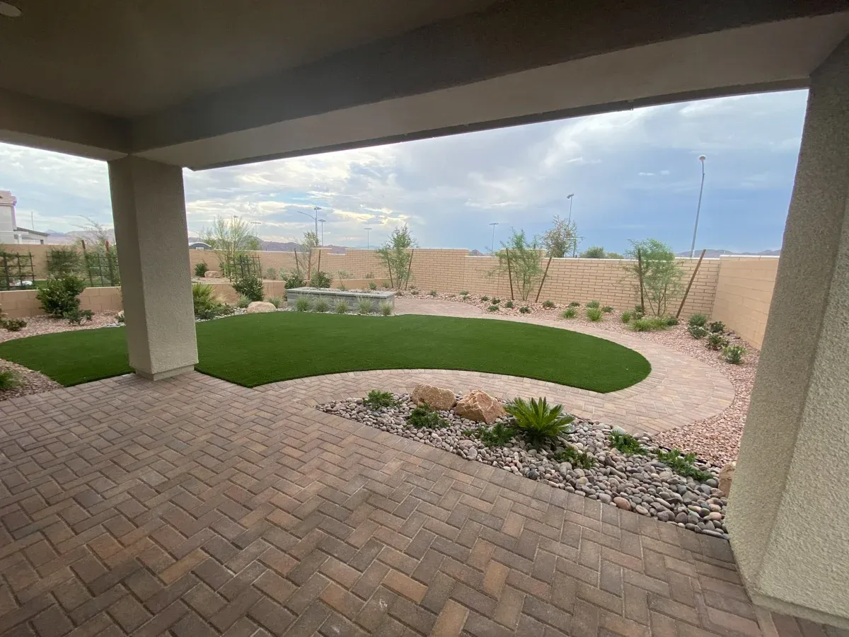 Artificial turf lawn installation in a covered patio area with hardscape pavers and desert landscaping elements.