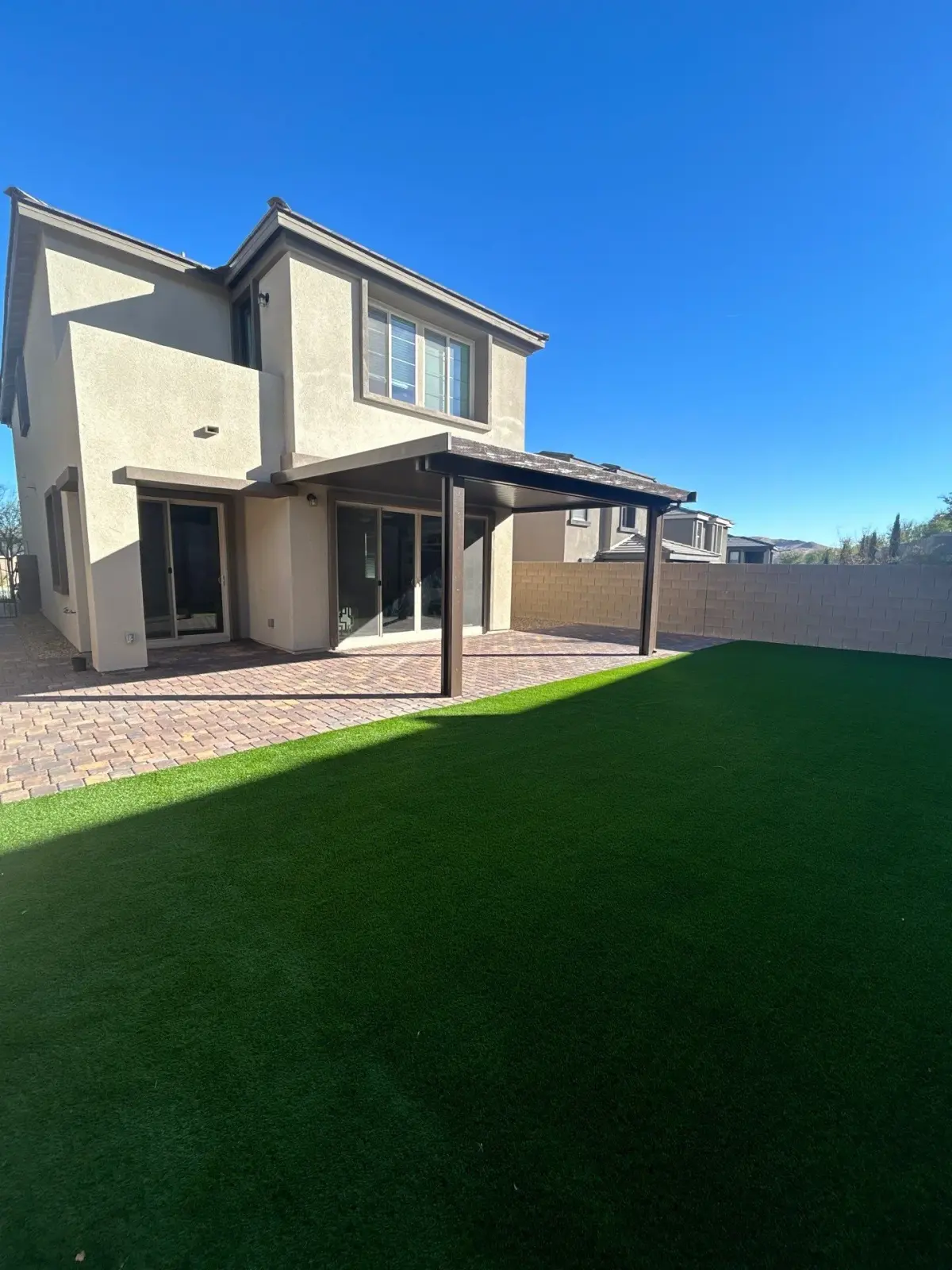 Artificial turf lawn installation in a residential backyard with modern hardscape patio and contemporary house.