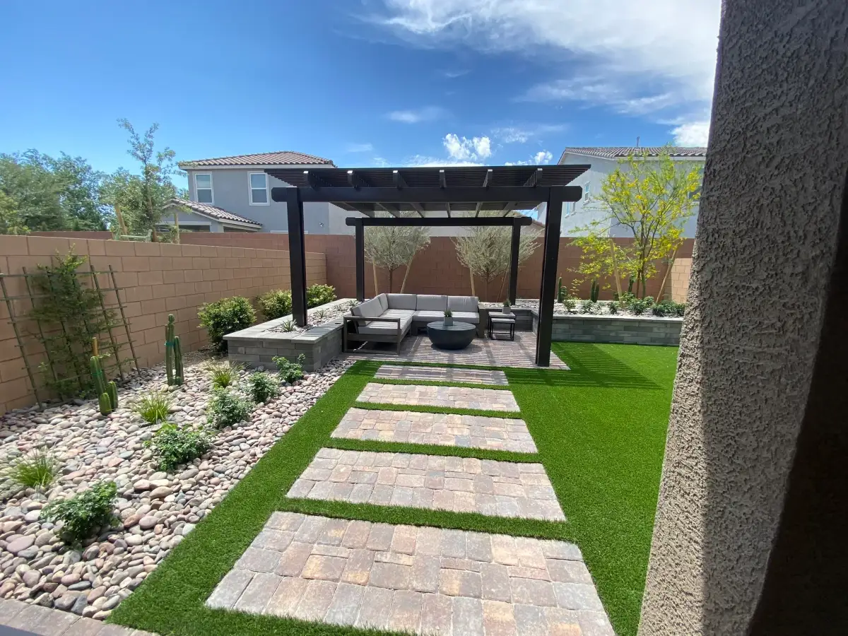 A modern hardscape patio and pergola installation in a residential backyard with artificial turf, pavers, and integrated seating areas.