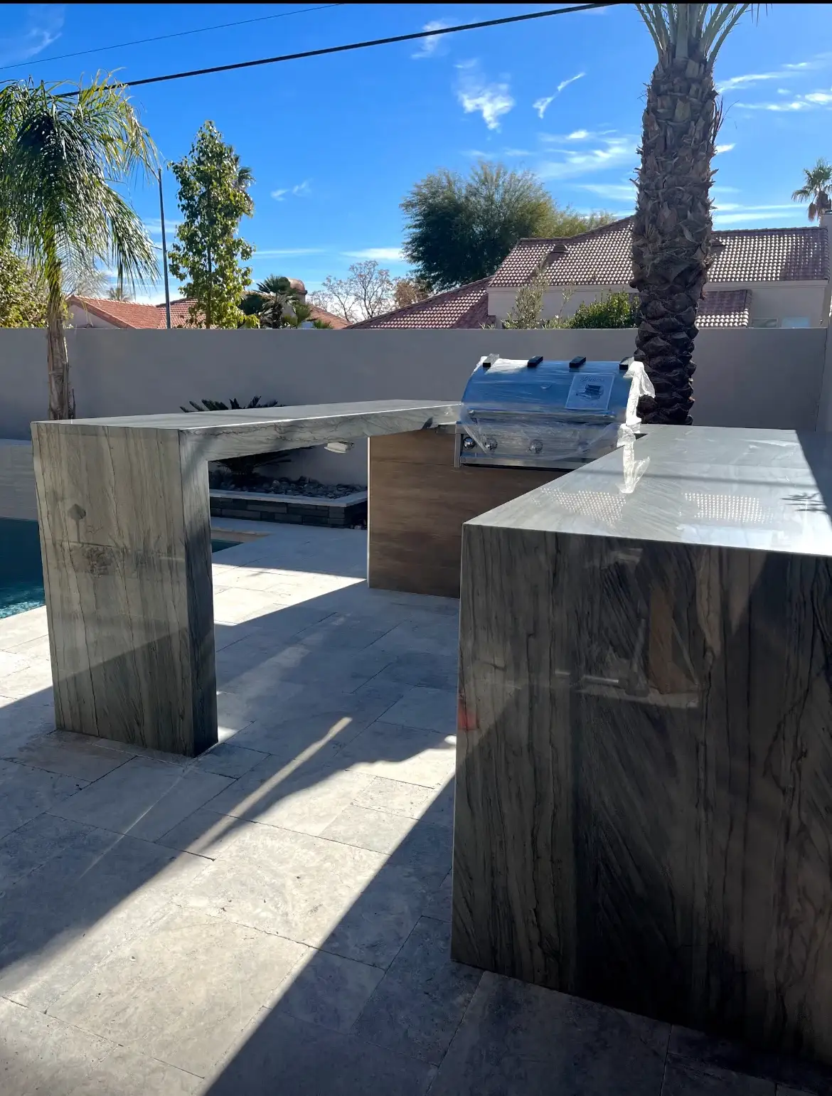 Outdoor kitchen hardscape installation with built-in grill and countertop surfaces in a residential backyard patio area.