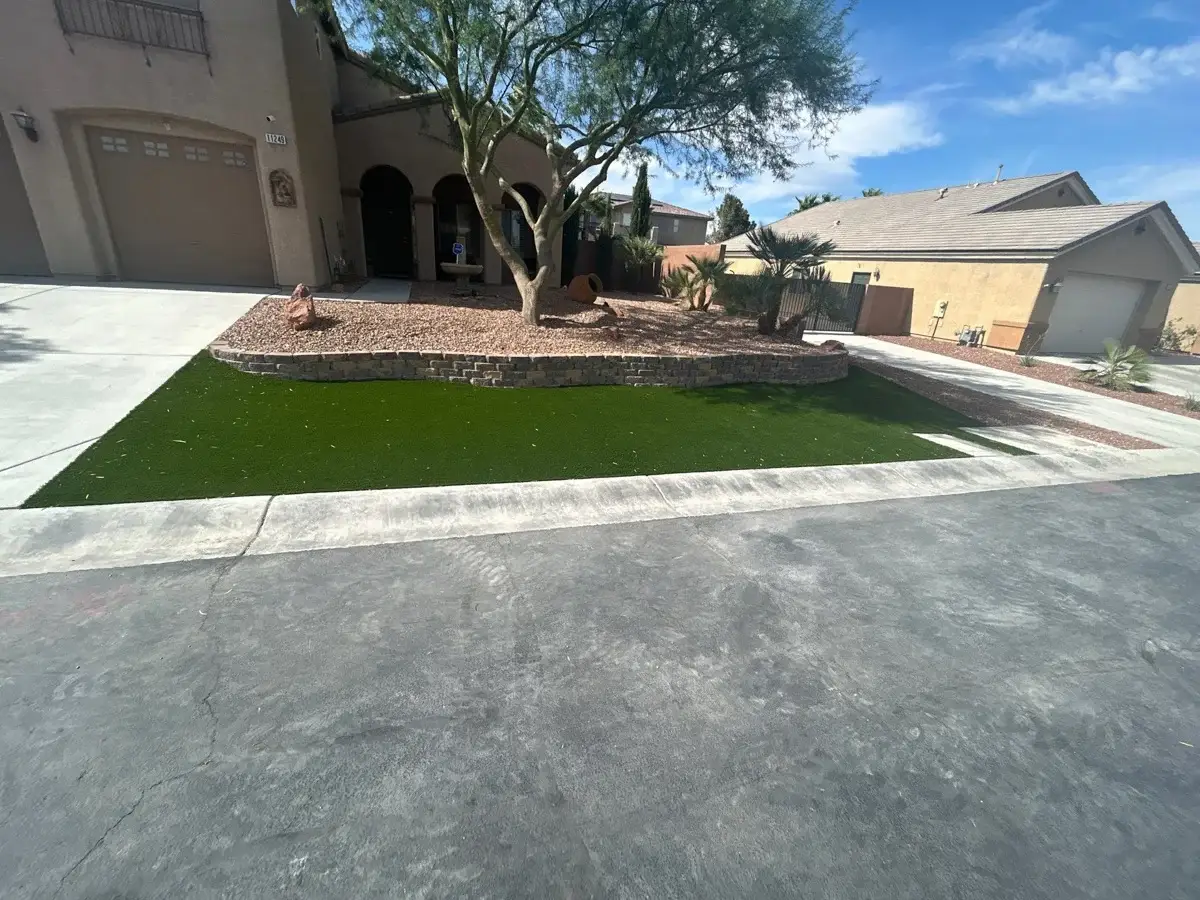 Newly installed artificial turf lawn with retaining wall and mature tree in a residential front yard.