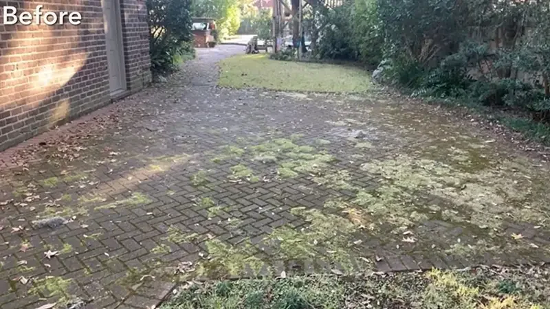 Pressure washing service on a brick driveway and paved surface in a residential setting, showing the before state with moss and algae buildup.
