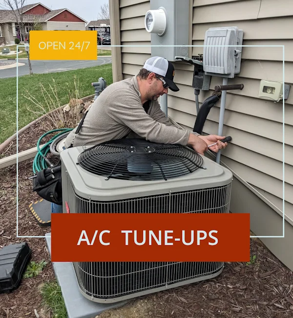 A technician performing an A/C tune-up on an outdoor air conditioning unit mounted on the side of a residential home.