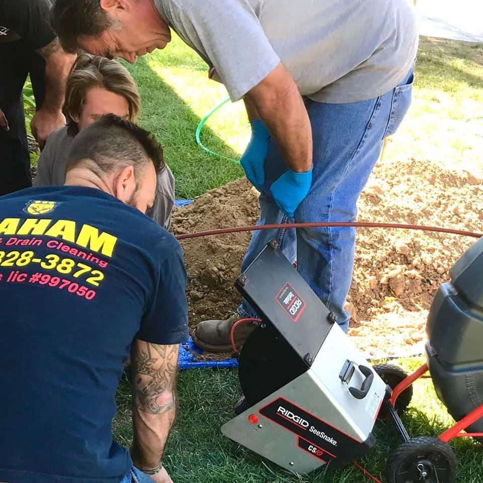 Drain cleaning equipment and snake tool being used during an active plumbing service in a residential outdoor setting.
