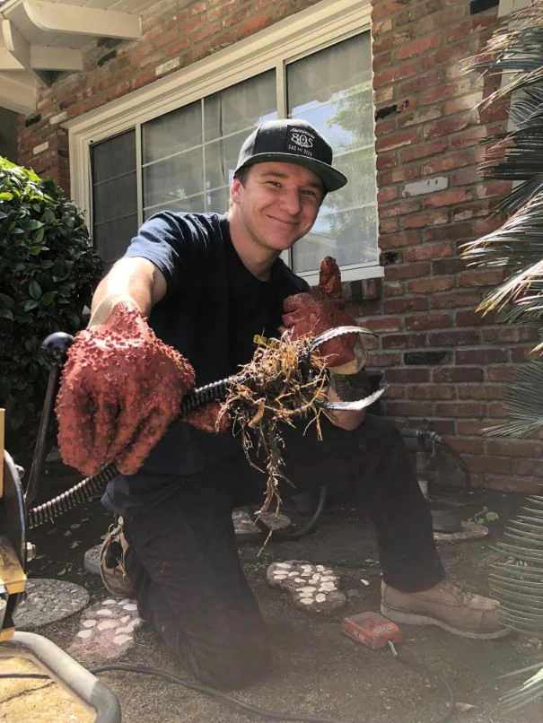 A person holding extracted roots and debris from a clogged drain or pipe during drain cleaning service in a residential exterior courtyard.