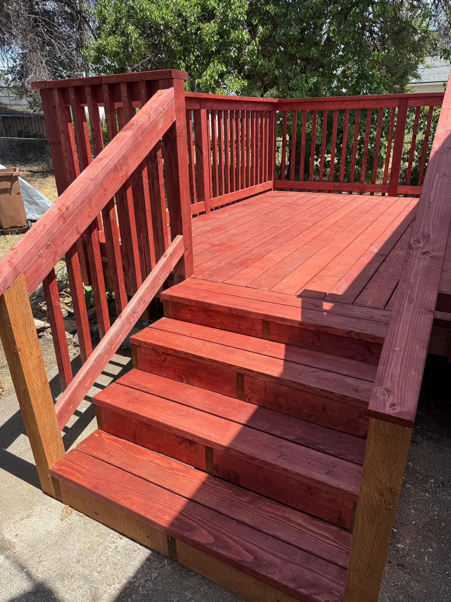 A custom red-stained wooden deck with stairs and railings in a residential exterior setting.
