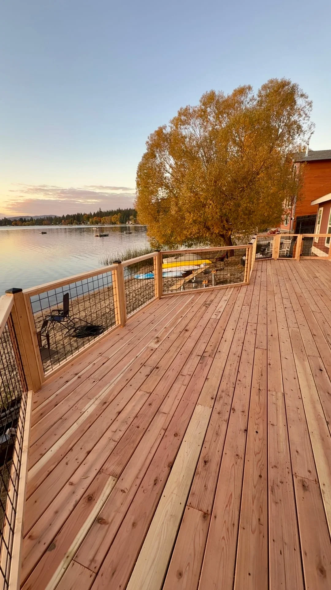A custom wooden deck with metal railing in a waterfront residential setting at golden hour.