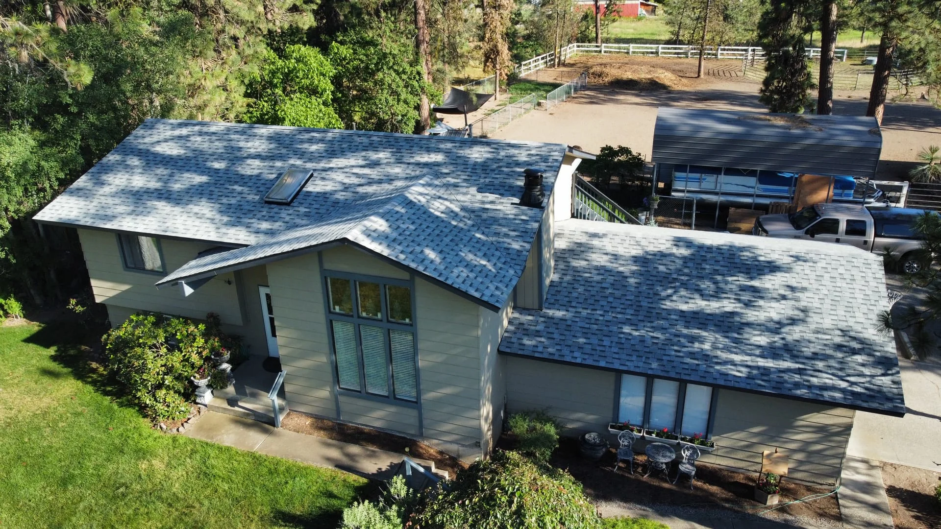 New roof installation with blue asphalt shingles on a residential home surrounded by forest and landscaping.