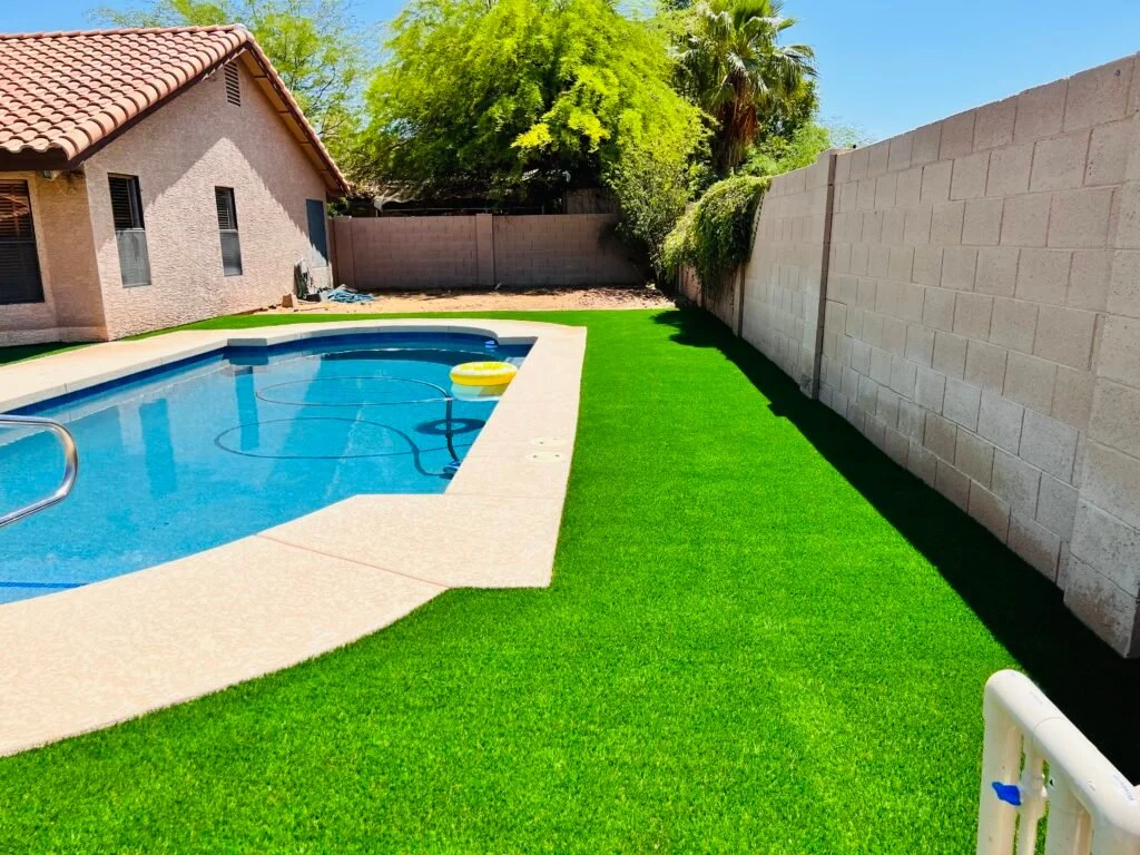 Artificial turf installation in a residential backyard with pool and patio.