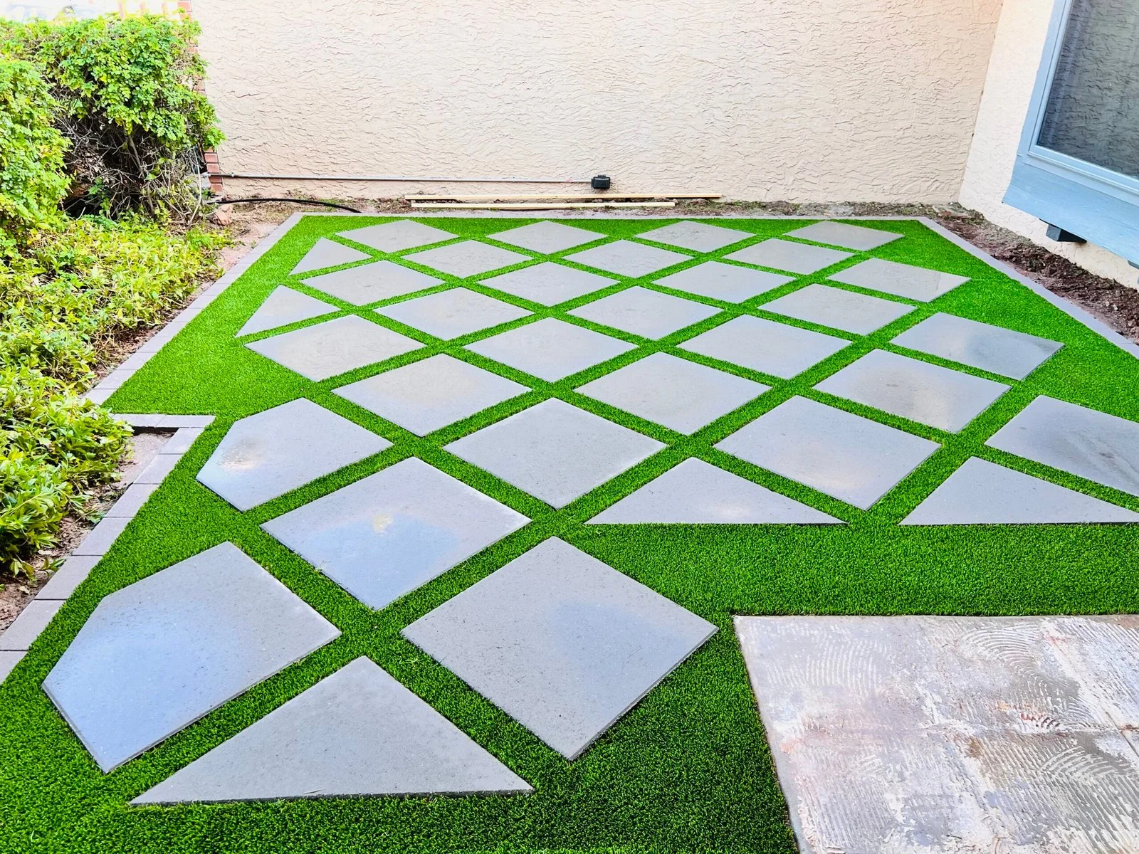 Artificial turf installation with decorative concrete pavers in a diamond pattern in a residential backyard setting.