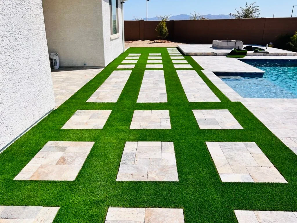 Artificial turf installation with decorative stone pavers in a geometric pattern alongside a residential pool and patio area.
