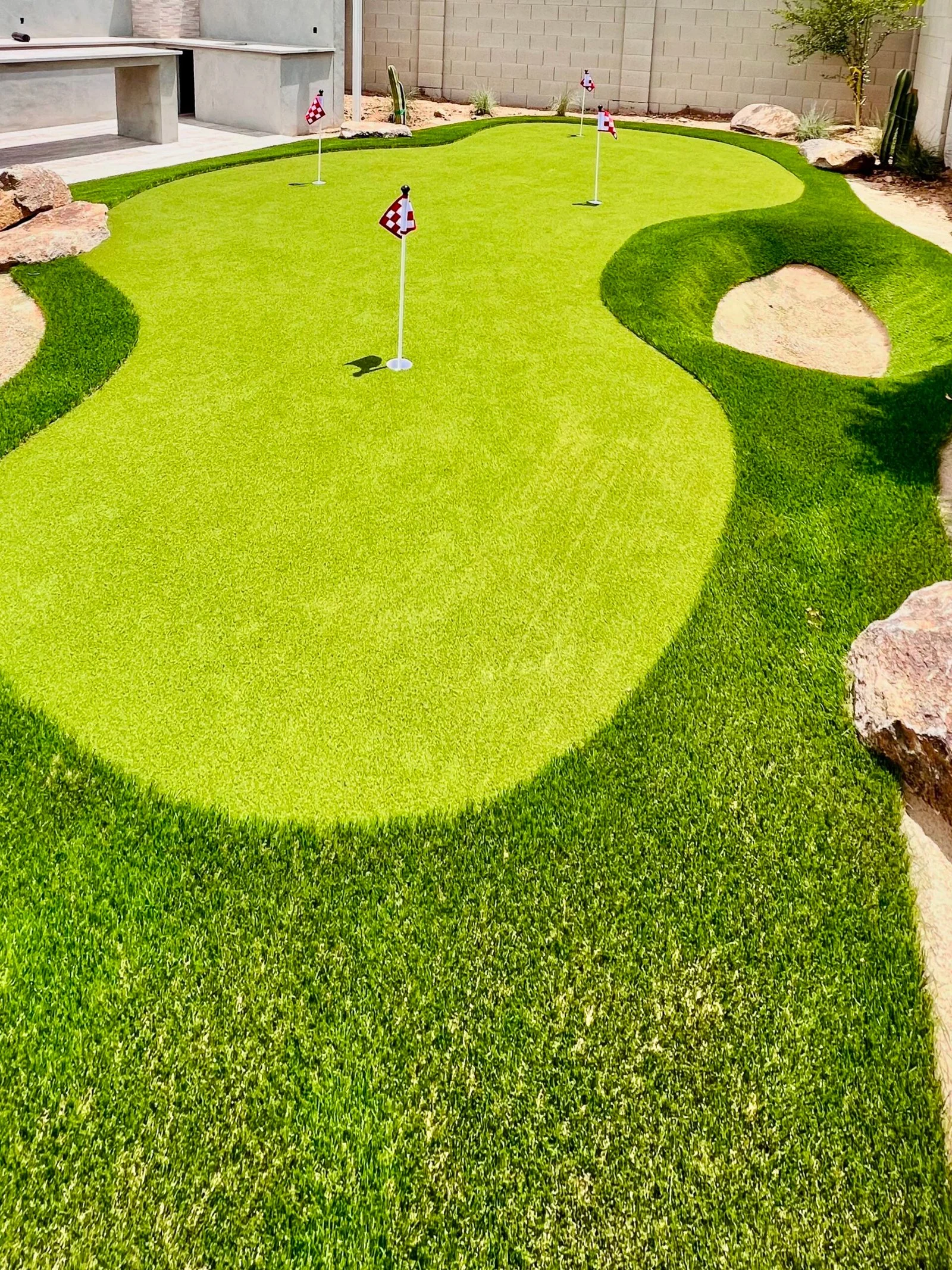 Artificial turf installation with integrated putting green and sand bunkers in a residential backyard setting.