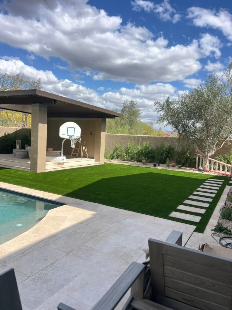 Artificial turf lawn installation in a modern backyard with pool, patio, and pool house.