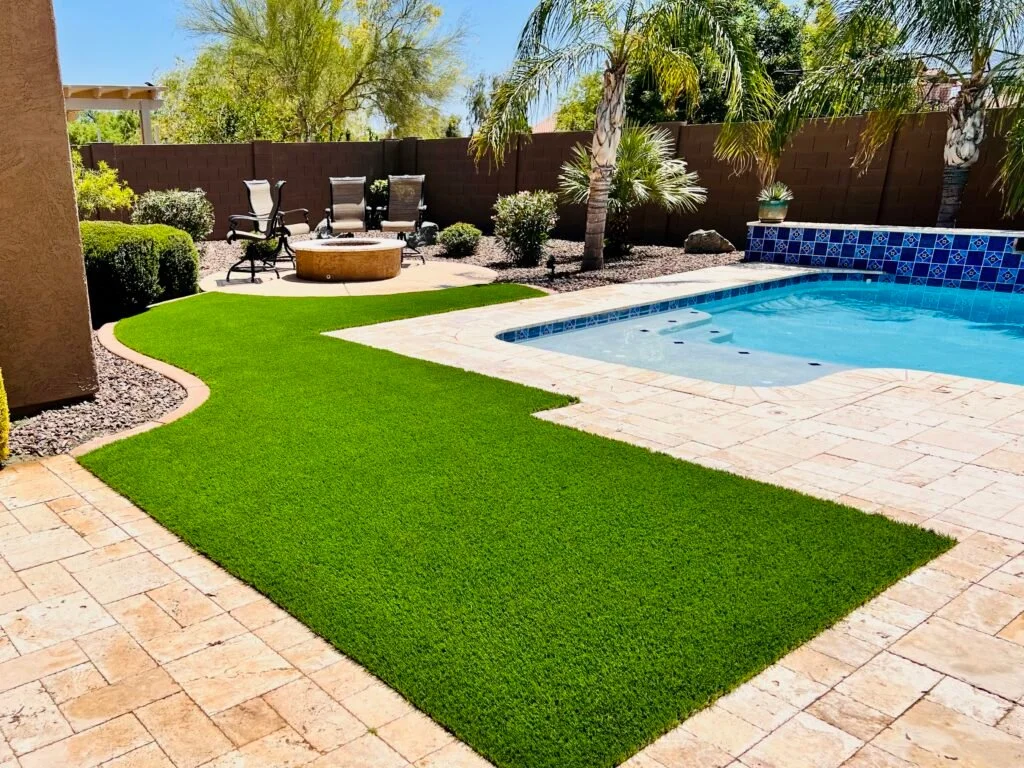 Artificial turf lawn installation in a residential backyard with pool and patio.